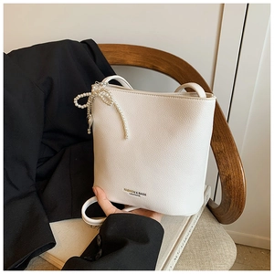 Close-up of white bucket bag featuring litchi texture and elegant pearl bow accessory