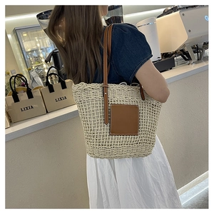 Detail of woven straw tote bag featuring brown leather shoulder straps and patch