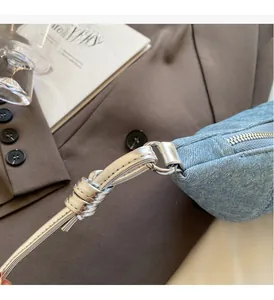 Close-up of polished silver hardware and knotted strap on light blue denim crescent bag