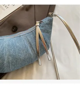 Detail of light blue denim croissant bag featuring smooth silver zipper and fringe tassel