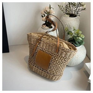 Detailed texture of woven straw tote bag with brown leather handles and drawstring liner