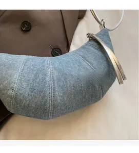 Detail shot of blue denim croissant bag texture with silver rings and leather zipper pull