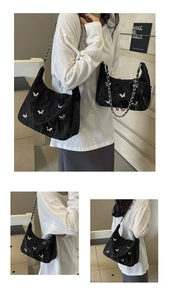 Detail of black pleated shoulder bag featuring silver butterfly patches and chain strap