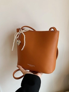 Brown orange leather bucket bag with litchi texture and pearl bow charm on shoulder strap