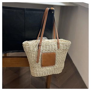 Detail of woven straw bag showing texture, leather patch and brown shoulder strap on chair