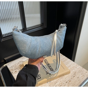 Close-up of quilted light blue denim croissant bag with silver metal strap and long tassels