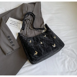 Detail of black pleated shoulder bag featuring metal butterfly charms and chain strap