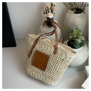 Detail of woven straw tote bag featuring brown leather patch and drawstring lining