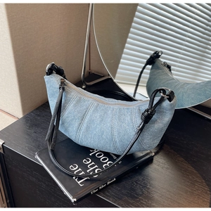 Detail of light blue denim croissant bag with pleated texture and leather knot strap