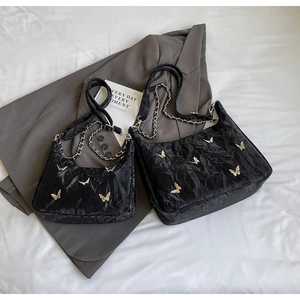Detail of black glossy crinkled tote bags with gold butterfly on grey blazer