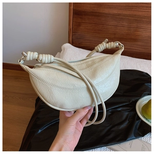 Detail of a creamy white crescent bag with wrinkled texture and knotted rope handle design
