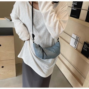 Detail of light blue denim croissant bag featuring pleated seams and slim leather strap