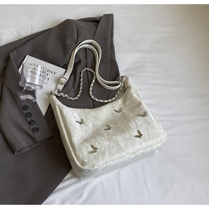 Macro shot of cream-white wrinkled fabric bag with silver butterfly charms and chain strap