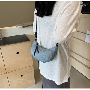 Close-up of light blue denim croissant bag with stylish knotted strap detail on person