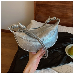 Close-up of a silver crescent-shaped leather handbag with unique knotted metal hardware