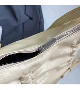 Dettaglio della cerniera in metallo argento e della pelle beige plissettata della borsa