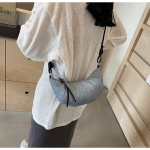 Detail of light blue denim croissant bag featuring knotted strap and twill texture