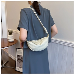 Detail of cream pleated crescent bag featuring intricate braided knot shoulder strap