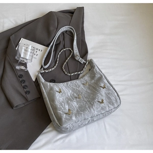 Detailed texture of silver crinkled shoulder bag with golden butterfly accents and chain strap