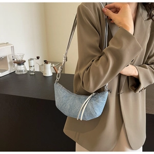 Detail of light blue denim croissant bag featuring silver woven strap and stitching