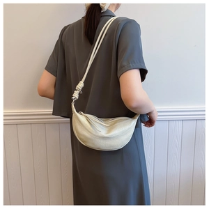 Detail of off-white crescent bag with crocodile texture and knot decoration on strap