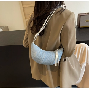 Detail of light blue denim croissant bag with silver knotted strap on model