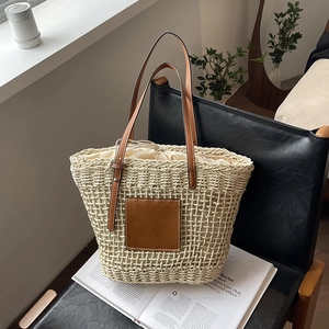 Woven straw tote bag with brown leather handles and drawstring lining on a chair