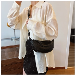 Close-up of black pleated leather crescent bag with metal ball detail and knotted strap
