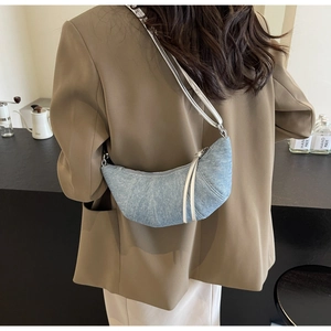 Detail of light blue denim croissant bag shown with model in brown blazer