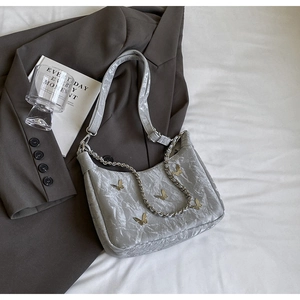 Close-up of light grey pleated shoulder bag with gold butterflies and silver chain link
