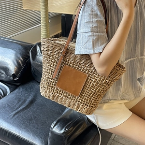 Handwoven straw tote bag with brown leather patch and shoulder straps on a casual model