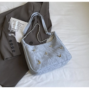 Close-up of light gray pleated tote bag featuring golden butterfly buckles and metal chain