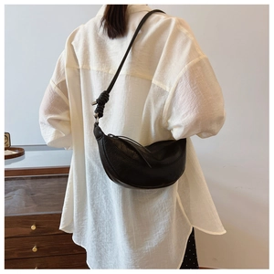 Detail of black croissant shoulder bag with pleated texture and sphere knot on strap