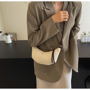 Detail of a minimalist cream croissant bag with dark brown cord straps worn by a model