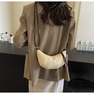 Detail of a minimalist cream canvas croissant bag with leather strap on a shoulder