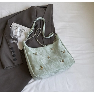 Close-up of mint green pleated tote bag featuring delicate metal butterfly decorations