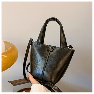 Detail of a black pleated bucket bag showing the glossy texture and dual handle design