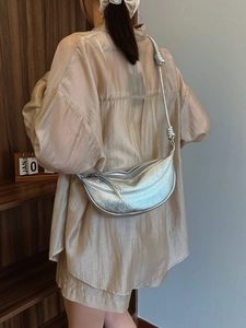 Silver metallic crescent crossbody bag with knotted strap shown on an elegant model