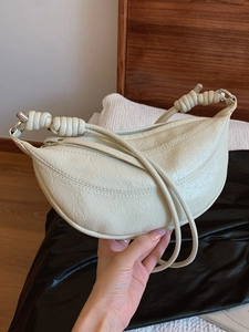 Cream colored pleated dumpling bag with knot detail strap shown in hand as shoulder bag