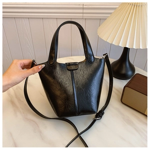 Detailed view of black bucket bag showing shiny pleated leather texture and sleek handle