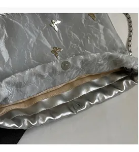 Detalle de bolso cubo plateado con mariposa metálica y cierre magnético de estilo