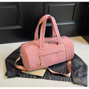 Detalle de bolsa de viaje cilíndrica rosa con asas sobre fondo de cuero negro rugoso