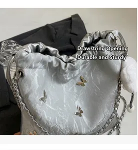 Detalle del bolso de hombro plateado con cordón, mariposas metálicas y asa de cadena