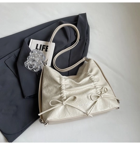 Dettaglio delle pieghe in pelle color crema e dei fiocchi decorativi su una borsa minimal