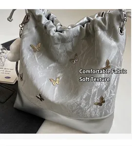 Detalle del bolso de cubo plateado con cordón, mariposas 3D y suave pompón de peluche