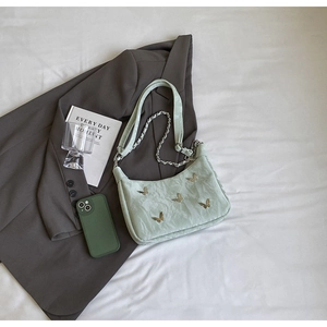 Detail of light green crescent bag with golden butterfly charms and ruched texture