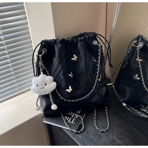 Detail van zwarte bucket bag met trekkoord, zilveren vlinders en wolkenhanger