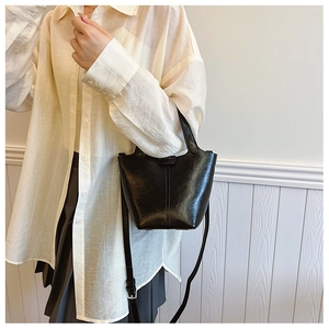 Detail of black bucket bag with vintage texture and adjustable strap on a model
