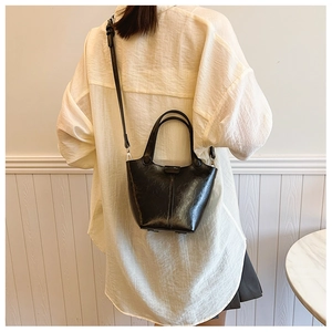 Detail shot of a black glossy bucket bag featuring dual handles and a long shoulder strap
