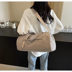 Detalle del bolso cilíndrico de nailon beige con correas reforzadas y clips metálicos